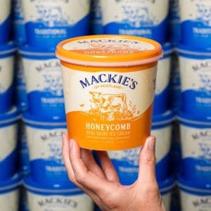Mackie's Honeycomb ice cream tub held by hand, stacked ice cream containers in background