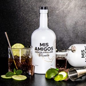 Mis Amigos Chocolate & Lime Tequila bottle with glasses and lime slices on a dark background